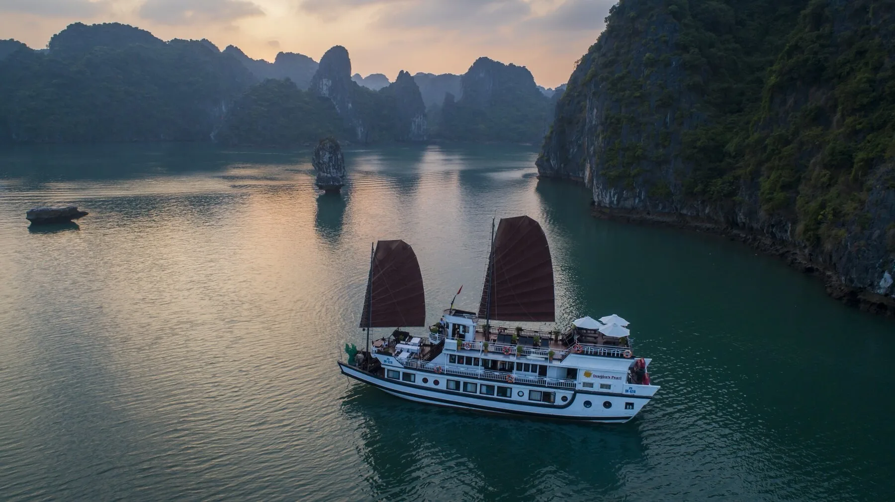 Dragon’s Pearl Junk cruising through Bai Tu Long Bay at sunset